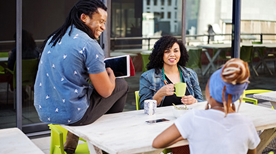 Three people gathered around a picnic table while smiling at each other  
