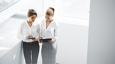 Two business women comparing notes on tablets