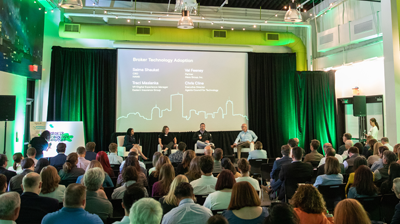 A conference with four speakers sitting on the stage while presenting to a crowd 