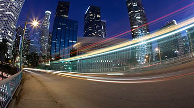 A road with light trails, city skyline in the background