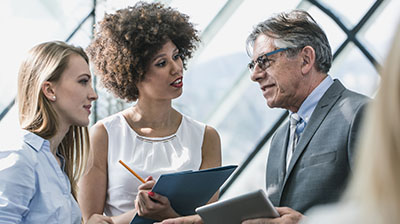 Two young businesswomen speaking with a businessman, one woman taking notes