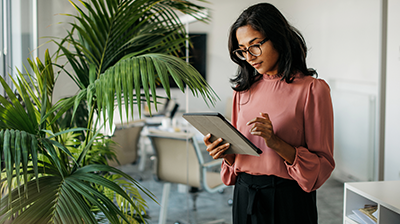 A woman standing next to a tall plant while using her tablet