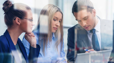 Two women and a man in a meeting working on a laptop