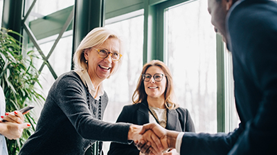 A group of people dressed in business attire while a man and a woman are shaking hands in the middle of the group 