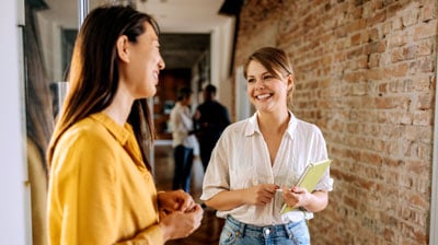 Two female colleagues talking in a hallway of modern office.