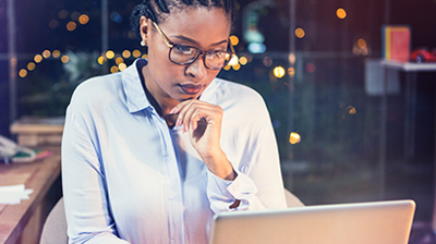 A woman wearing glasses, working on a laptop at night