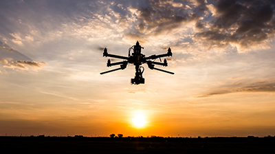Drone flying in the sky towards horizon during sunset