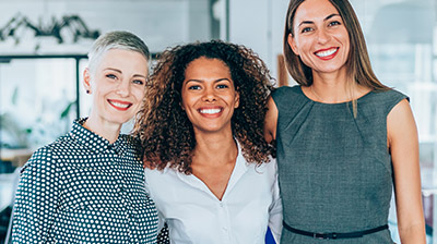 Three women dressed in business attire standing next to each other while smiling 