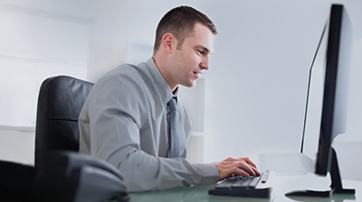 Man in business attire sitting at desk and typing on computer while smiling