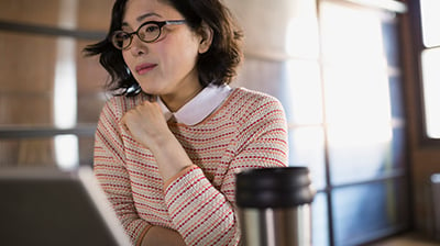 Woman dressed in business attire sitting and using a laptop with a portable coffee mug next to the laptop.