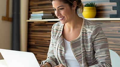 Woman in business attire smiling and using a laptop.
