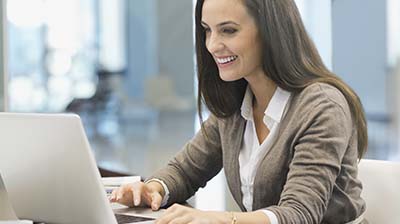 Woman in business attire sitting at a desk with an open laptop in front of her.