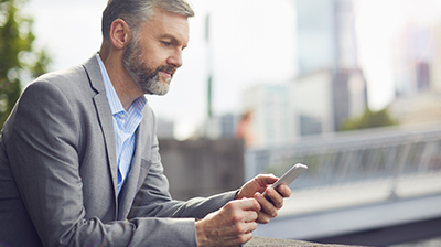 Man dressed in business attire sitting outside using a mobile phone.