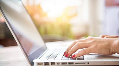 A woman's hands typing on a laptop keyboard