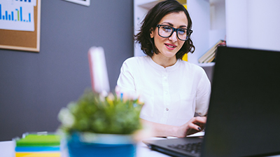 Woman sitting at desk in business casual attire using a laptop.